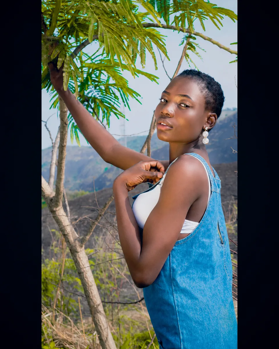 Outdoor lifestyle portrait of a young woman standing near trees and hills