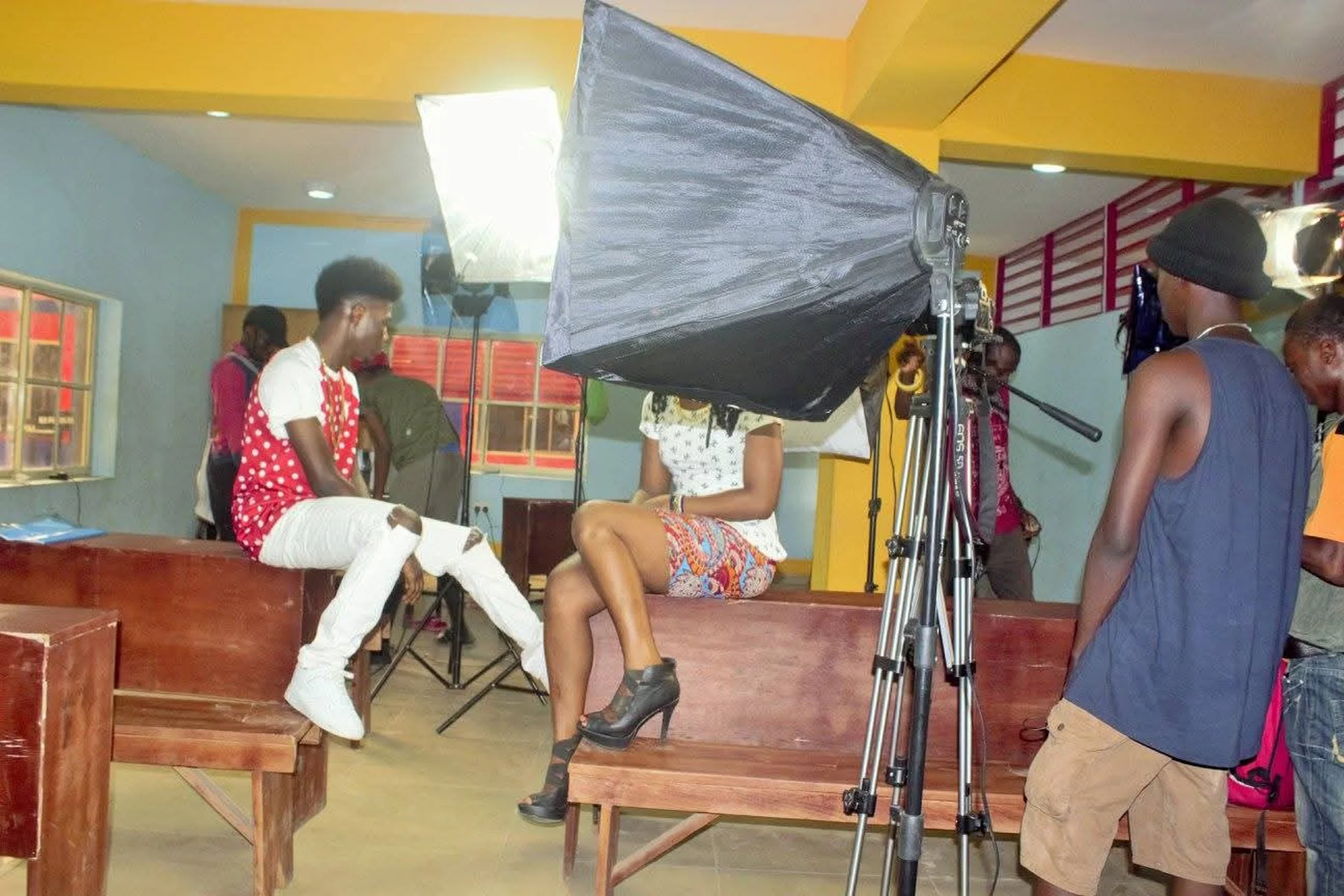 Behind-the-scenes photo of a video production setup with lighting gear, crew, and talent preparing for a scene indoors