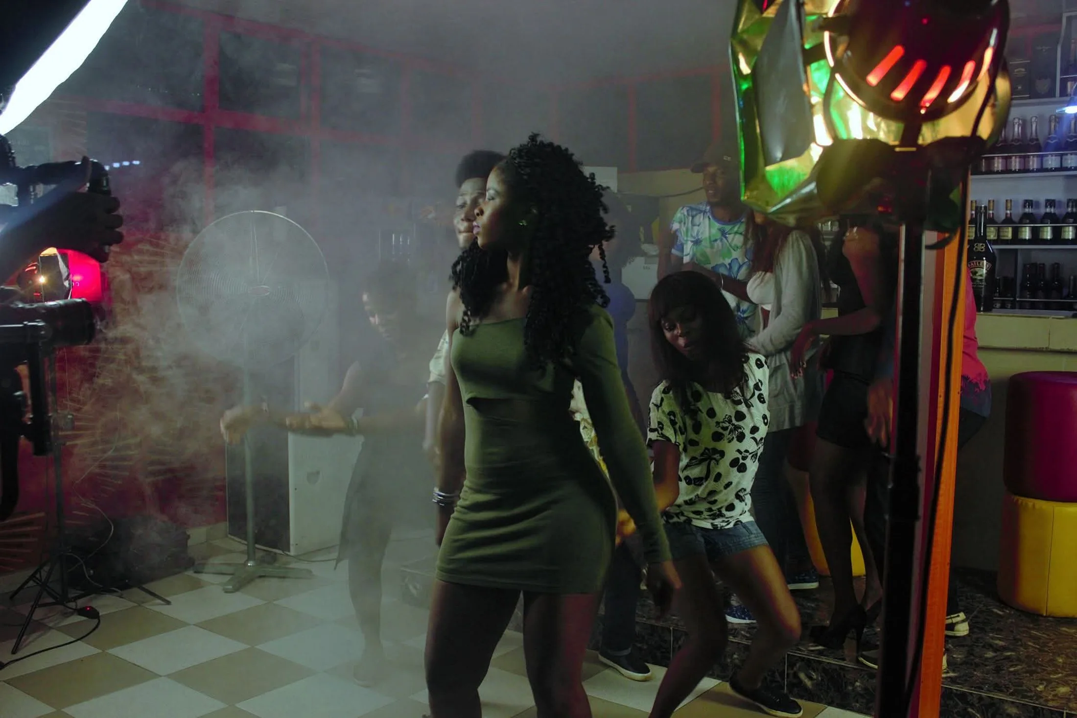 Behind-the-scenes image of performers and crew on a smoky, colorful music video set during active scene production