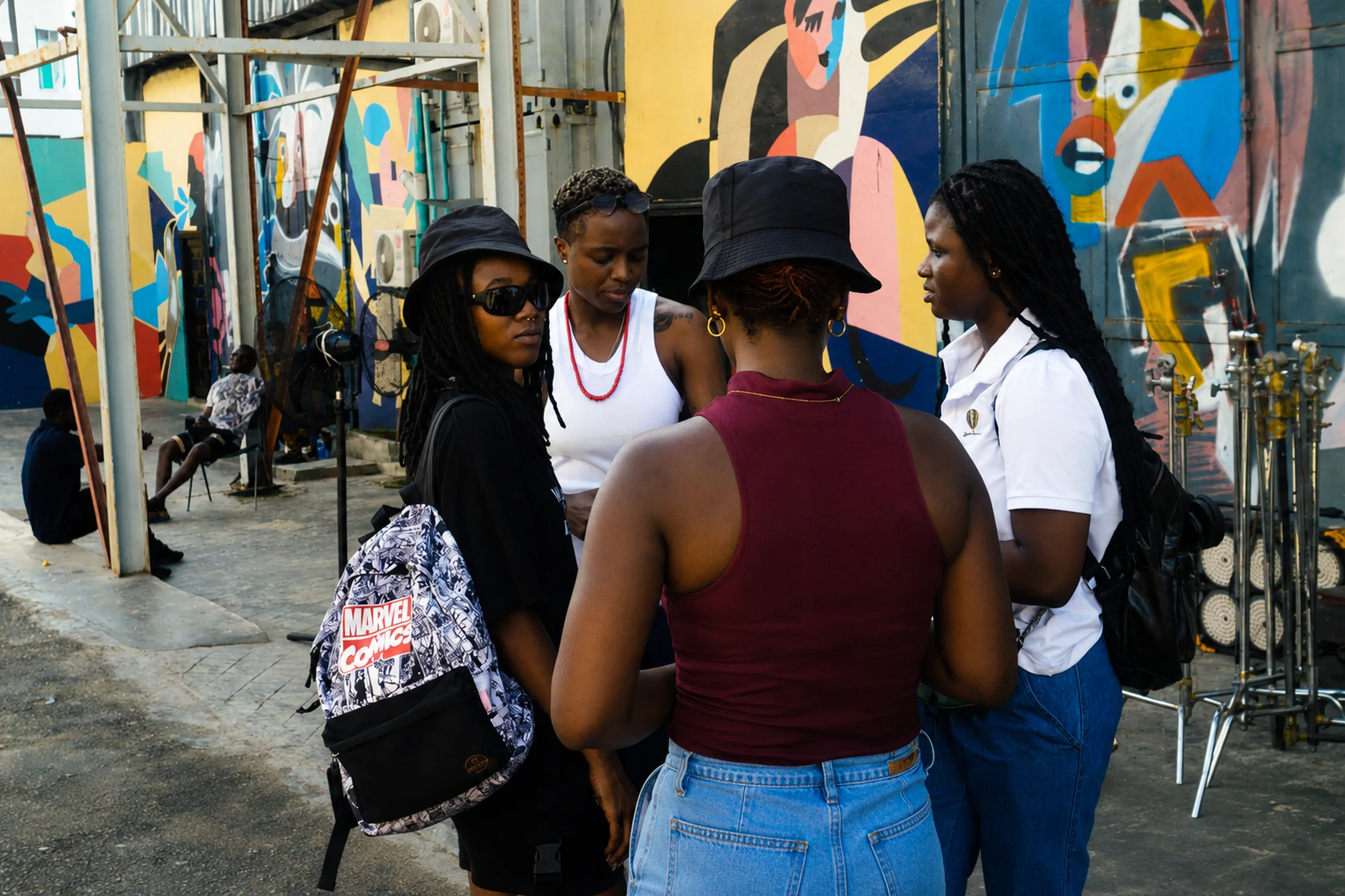 Behind-the-scenes team moment on a colorful outdoor set, showing cast and crew in conversation during production