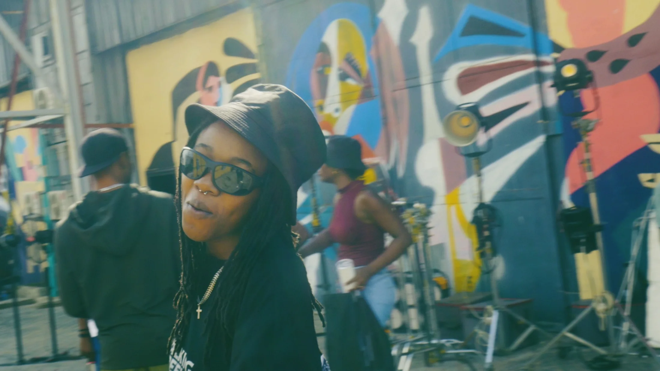 Candid behind-the-scenes portrait on set with vibrant mural background, showing personality and production energy